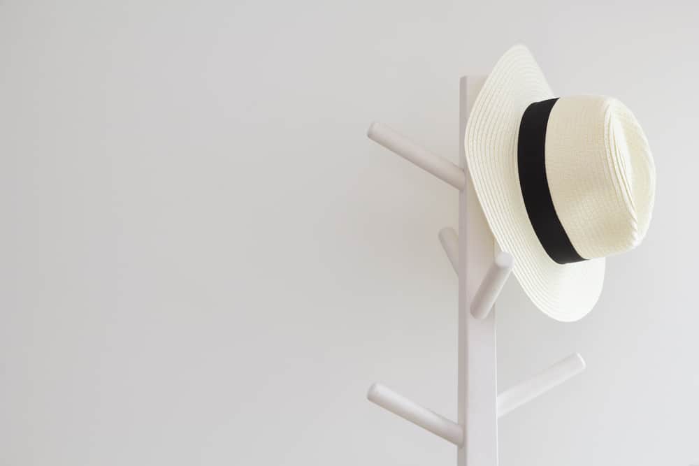 A white fedora hanging on a hat rack.