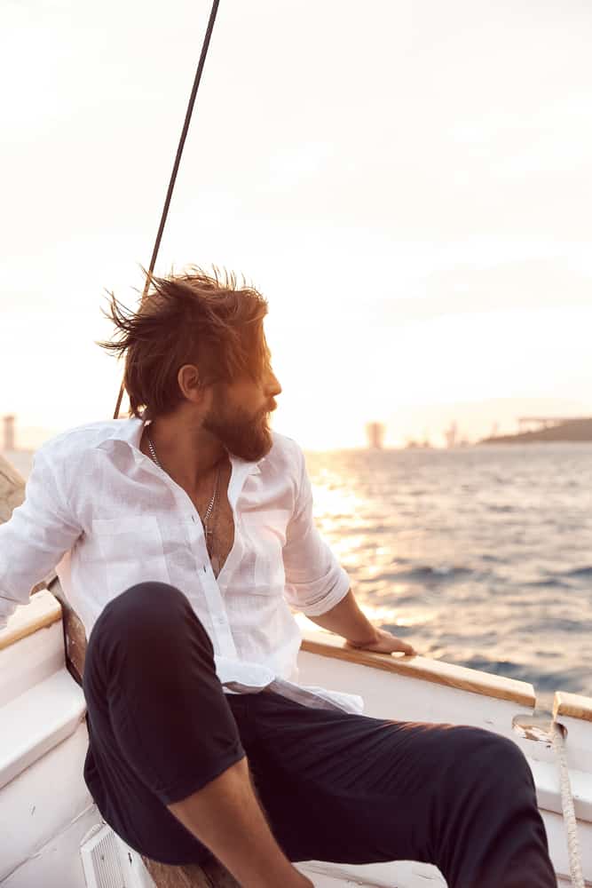 A man on yacht wearing a white linen shirt and blue pants.