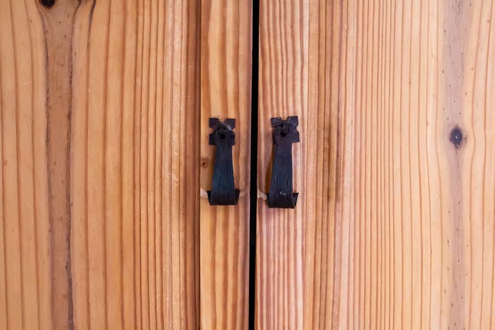 This is a close look at a wooden cedar wardrobe with iron pull handles on it.