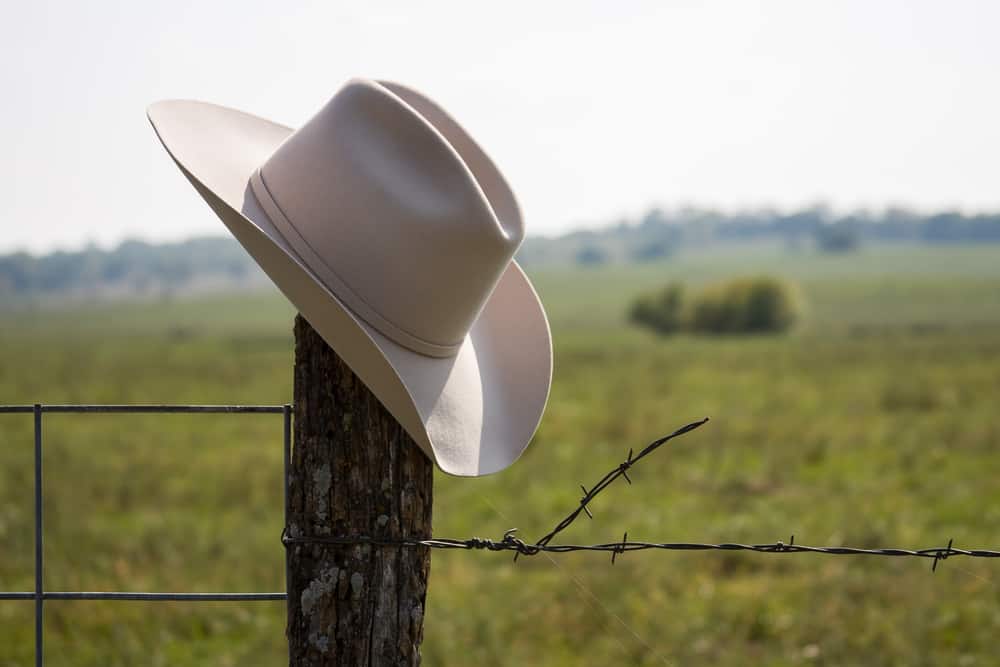 This is a close look at a beige cowboy hat on a wooden fence post.