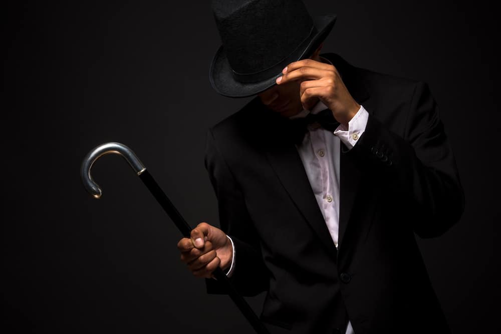 This is a man wearing a black tuxedo with a cane and a black top hat.