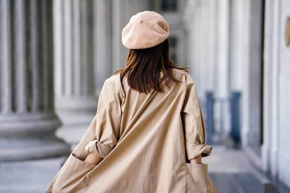 This is a close look at a woman wearing a beige beret with her tan trench coat.