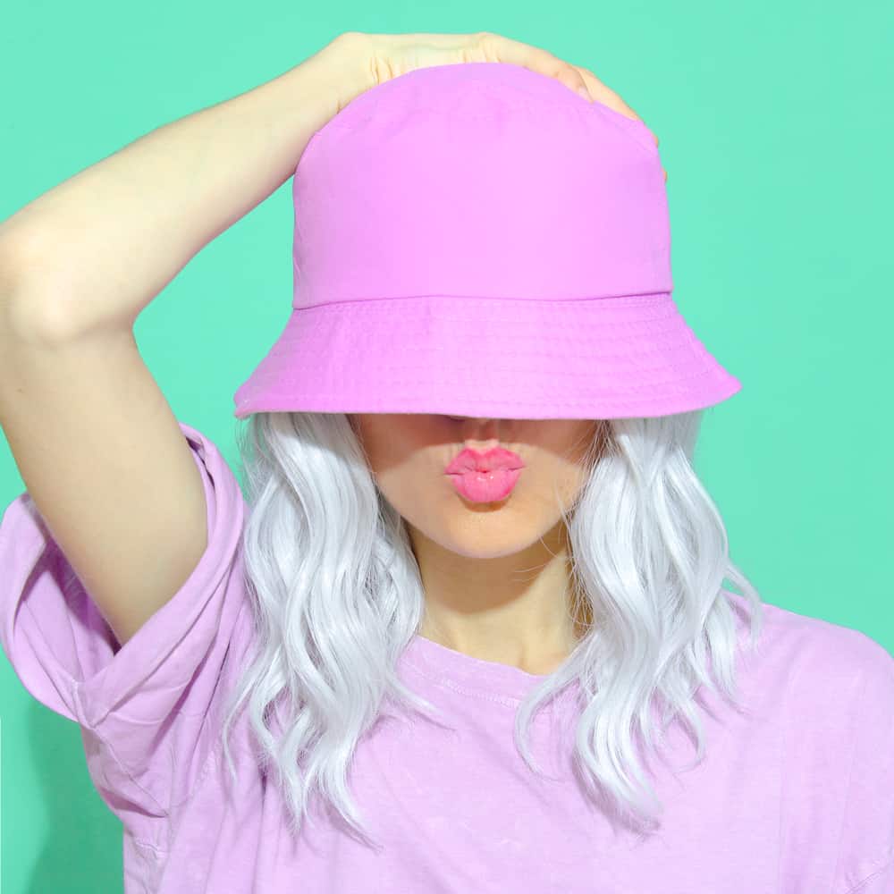 This is a woman wearing a purple shirt with her purple bucket hat and white hair.