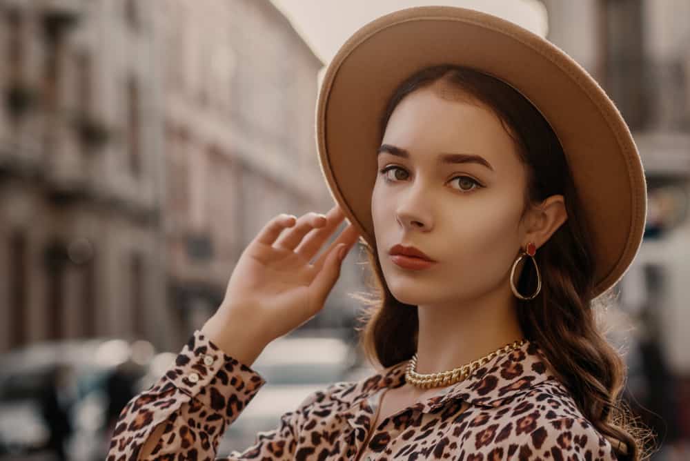 A woman wearing animal print blouse and a wide-brim fedora.
