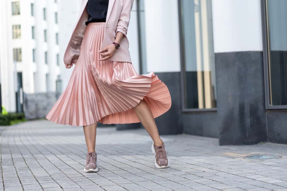 This is a close look at a woman wearing a pink pleated skirt with her sneakers.