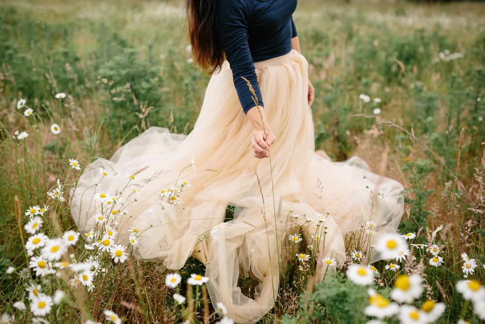 A woman wearing a tulle skirt standing on a field of flowers and grass.