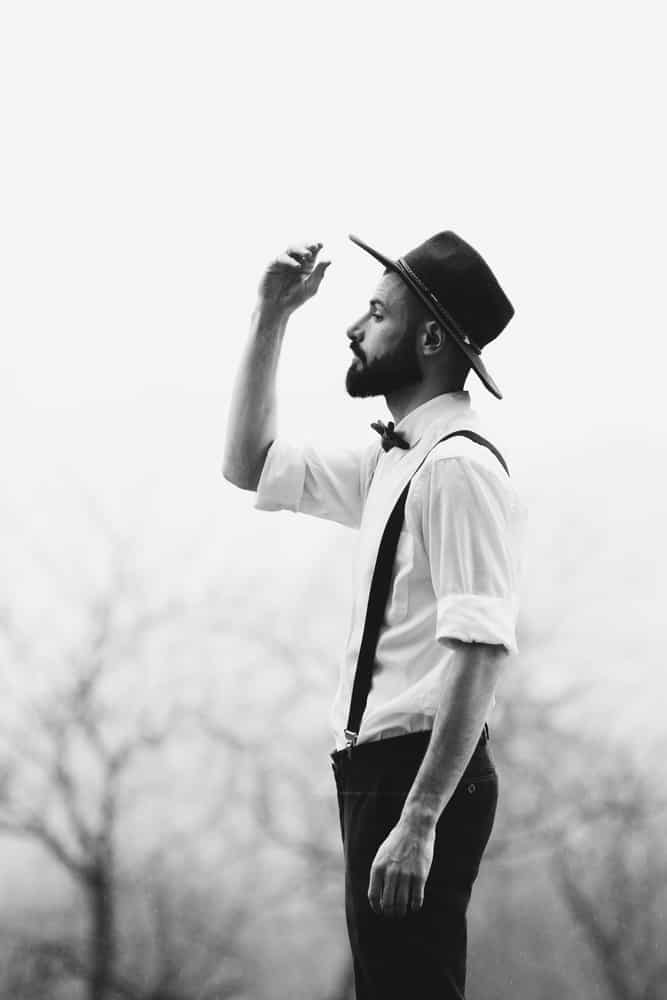 A black and white photo of a man wearing suspenders and a fedora.