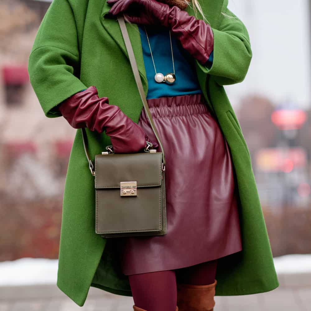 This is a woman wearing a red leather skirt with her green coat.