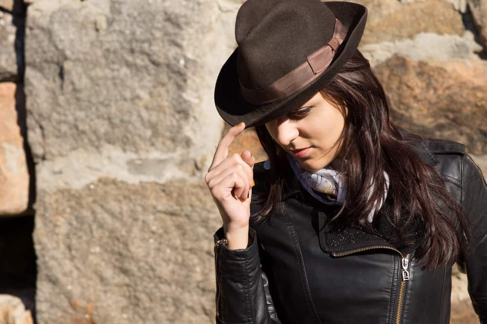 A woman wearing a black rider jacket with her brown fedora hat.
