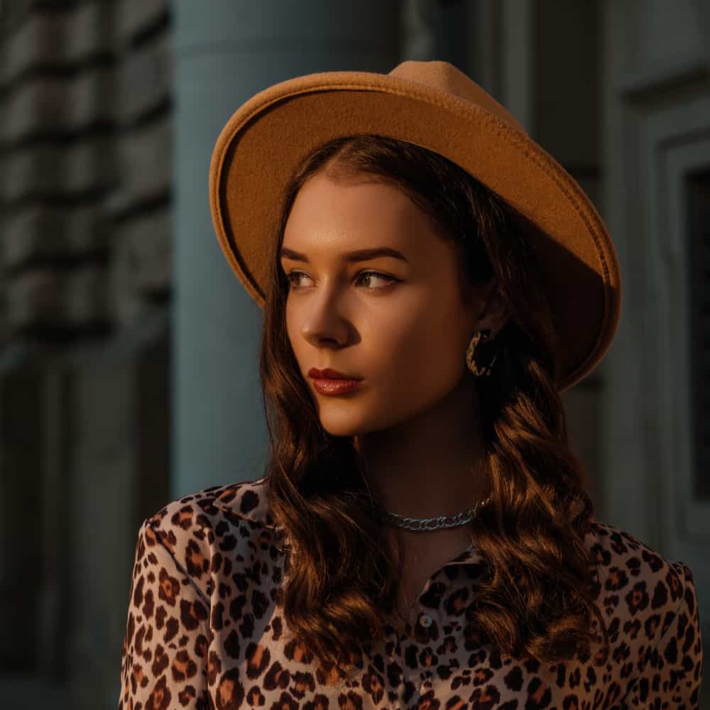 A woman wearing an animal print blouse with a fedora.