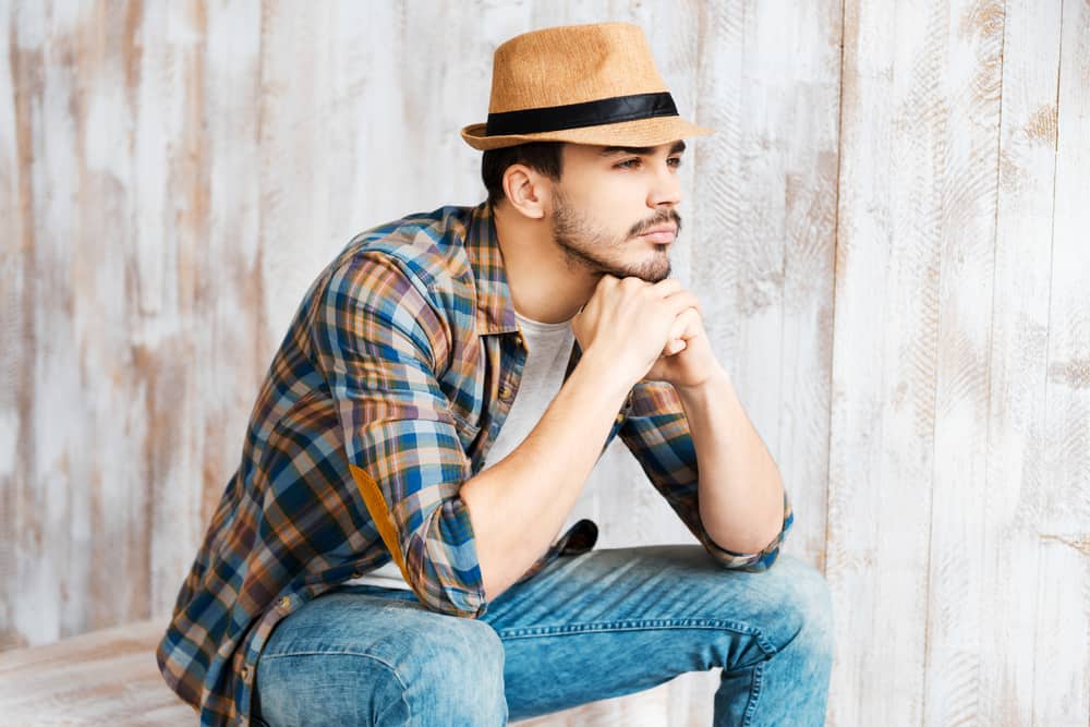 This is a man wearing a plaid shirt and blue jeans with his brown fedora.