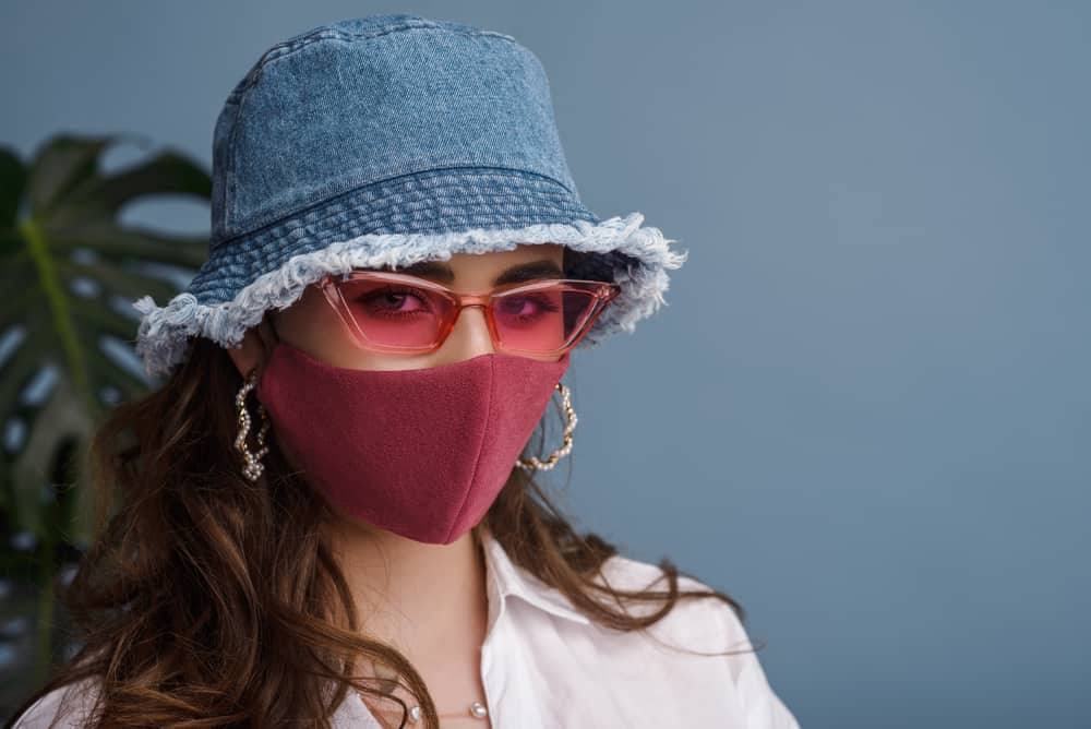 A woman wearing a denim bucket hat and a pink face mask.