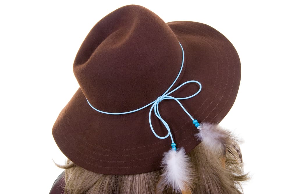 A woman wearing a brown fedora embellished with feathers.
