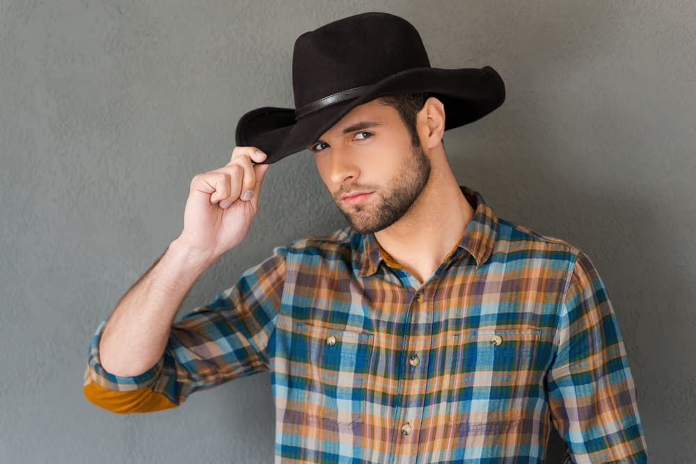 This is a man wearing a plaid shirt with his dark cowboy hat.