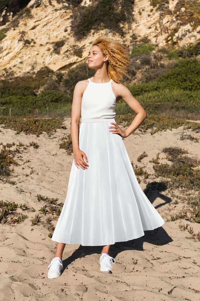 A woman wearing a white top, a white maxi skirt and a pair of white sneakers.