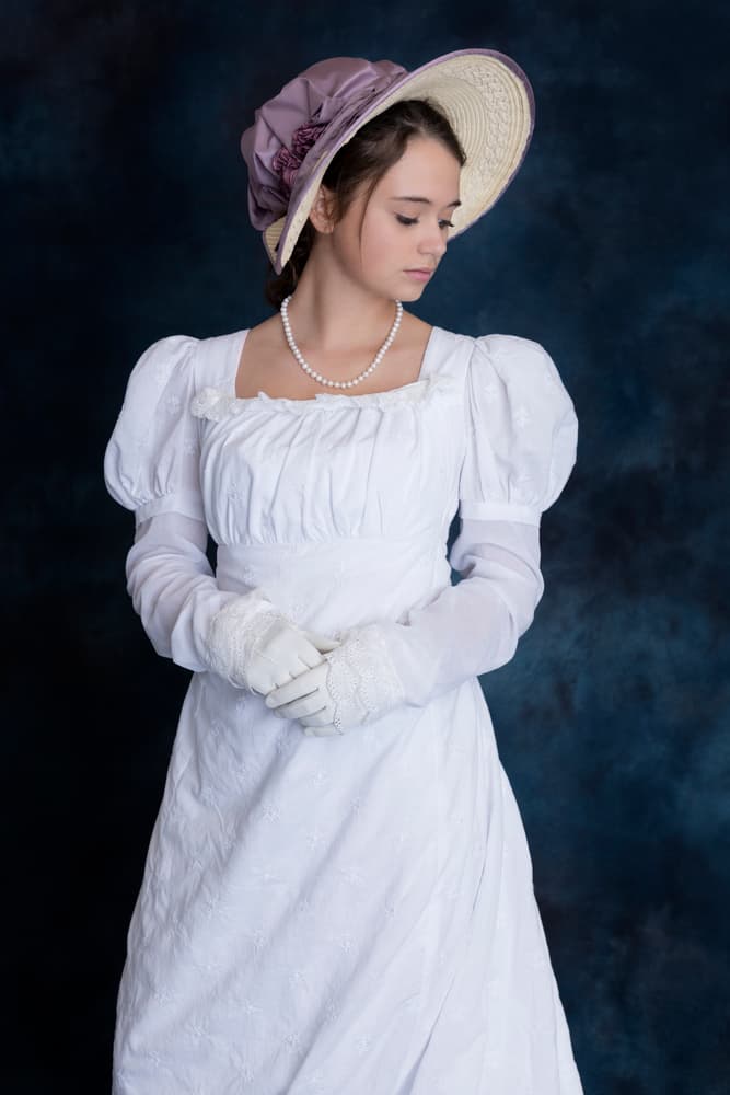 This is a woman wearing a white vintage dress topped with a bonnet hat.