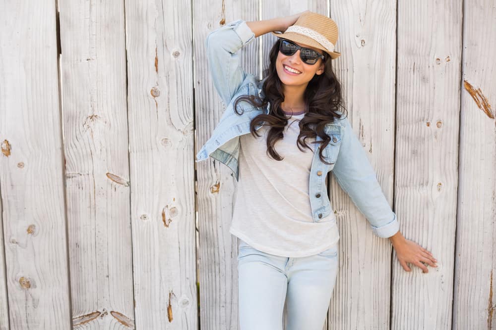 This is a woman wearing a denim jacket, a pair of sunglasses and a trilby hat.
